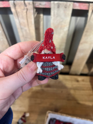 Small red and black figurine with 'KAYLA' on a keychain held by a hand against a blurred background.