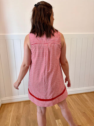 Person wearing a red and white checkered dress in a room with wooden flooring and white walls.