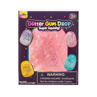Tartaruga Glitter GUM DROP Super Squishy! toy packaging on a white background. The box is dark purple with colorful text and shows a large pink glittery squishy ball in the center, surrounded by smaller multicolored glitter balls.