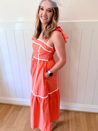 Woman wearing a coral dress with white trim against a white paneled wall.