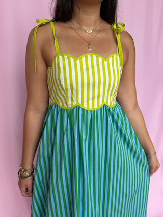 Person wearing a yellow and green striped dress against a pink background