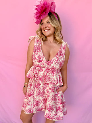 Woman wearing a pink floral dress and matching fascinator against a pink background