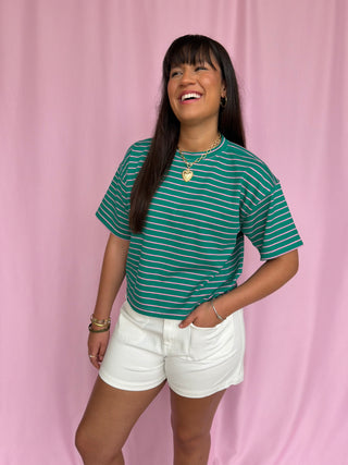 Woman wearing a green striped shirt and white shorts against a pink background