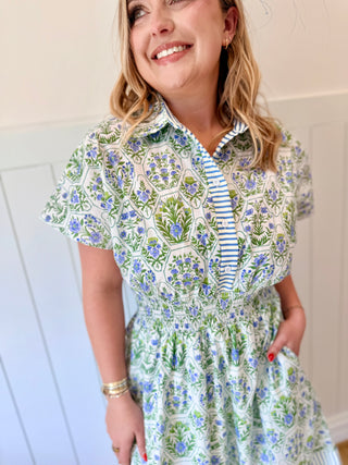 Woman wearing a floral dress with a striped collar against a white wall.