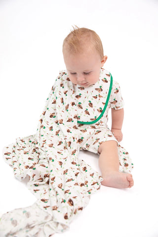 A baby sitting on a white studio background wearing a cream-colored footed sleeper with a brown and green woodland animal print and a green zipper.