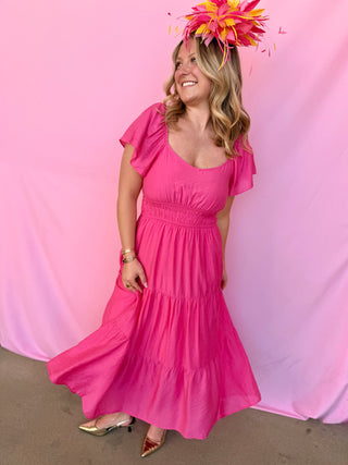 Woman in a pink dress with a floral headpiece against a pink background