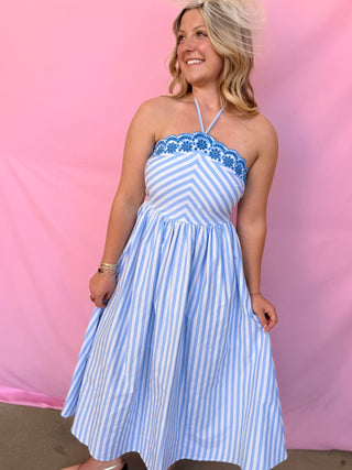 Woman wearing a blue and white striped dress with floral details against a pink background