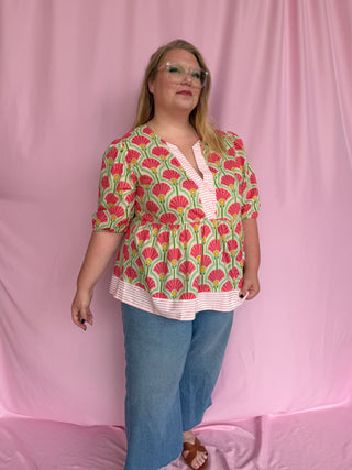 Woman wearing a colorful patterned blouse and blue jeans against a pink background