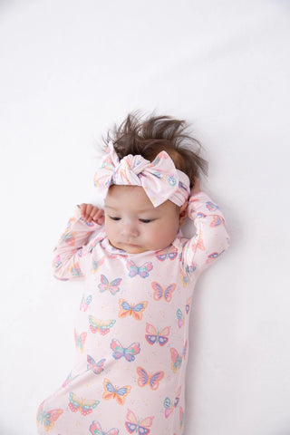 Baby wearing a pink butterfly-patterned outfit and headband on a white background