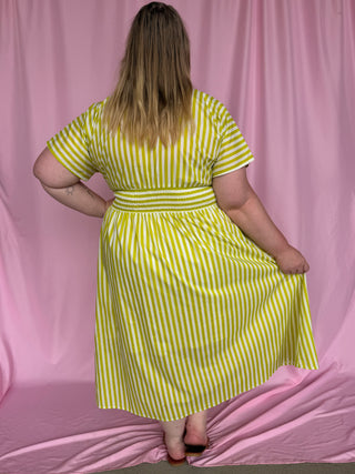 Person wearing a yellow and white striped dress against a pink background