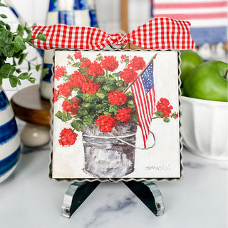 Decorative sign with red flowers, American flag, and checkered bow on a stand.