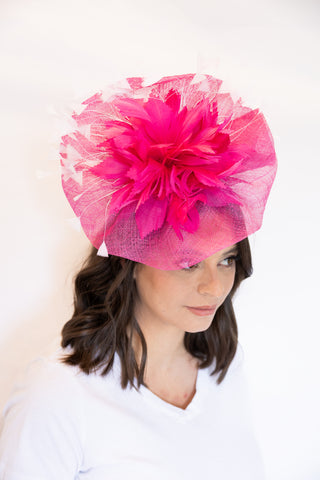 Woman wearing a bright pink fascinator hat against a white background