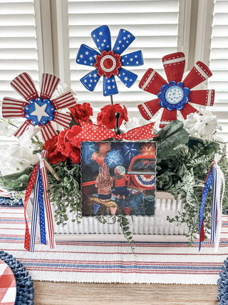 Decorative centerpiece with red, white, and blue flowers and a photo of a child in a red shirt.