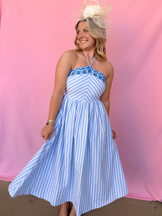 Woman wearing a blue and white striped dress with floral details against a pink background