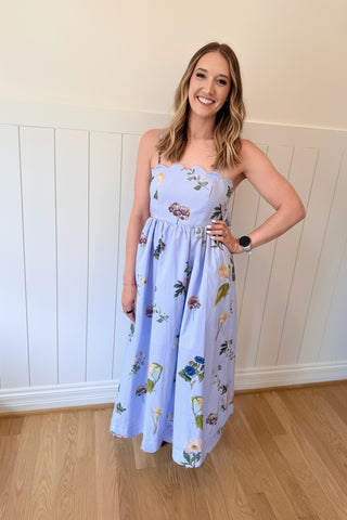 Woman wearing a floral dress and blue fascinator indoors.