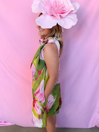 Woman wearing a floral dress and large pink flower hat against a pink background