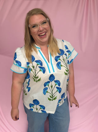Person wearing a white blouse with blue floral patterns on a pink background
