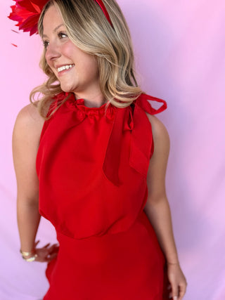 Woman wearing a red dress with bow details against a pink background