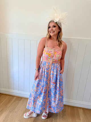 Woman wearing a floral dress with a large white headpiece against a white paneled wall.