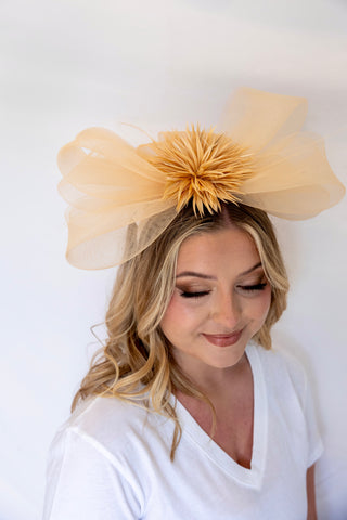 Woman wearing a large beige bow headpiece against a white background