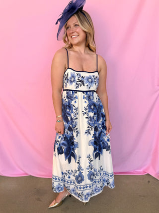 Woman wearing a floral dress with a blue hat against a pink background