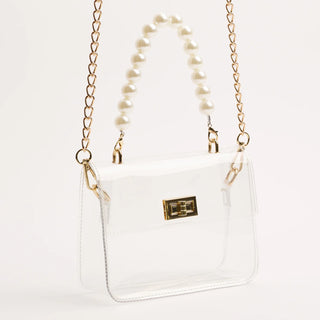 Clear handbag with gold chain strap and pearl necklace on a white background