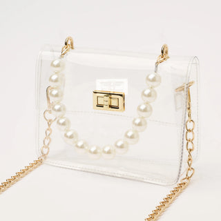 Clear handbag with gold chain and pearl-like accents on a white background