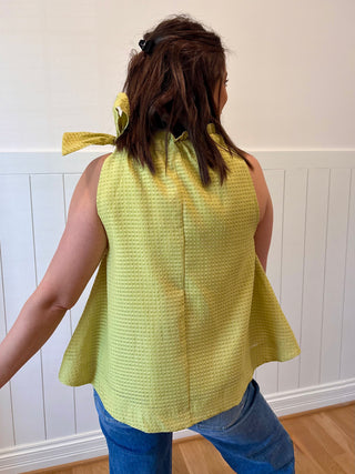 Person wearing a yellow sleeveless top with a white wall background