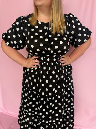 Person wearing a black dress with white polka dots against a pink background