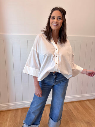 Woman wearing a white blouse and blue jeans standing against a white paneled wall.