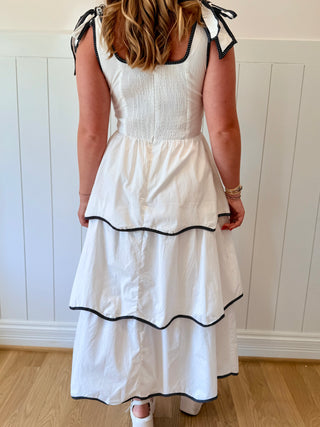 White dress with black trim worn by a person against a white paneled wall.