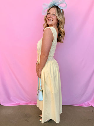 Woman in a yellow dress with a large bow headpiece against a pink and purple draped background