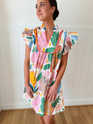 Woman wearing a colorful floral dress against a white wall.