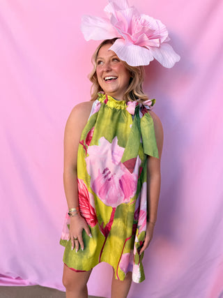 Woman wearing a floral dress and large pink hat against a pink background