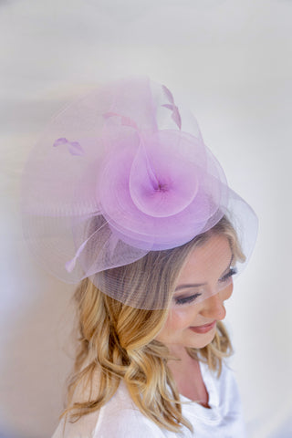 Woman wearing a light purple decorative headpiece with a veil on a white background