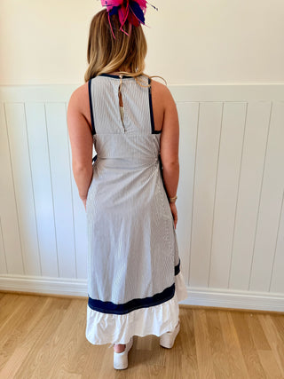 Woman wearing a white and navy striped dress with a headband against a white paneled wall.