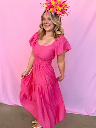 Woman wearing a bright pink dress and matching fascinator against a pink background