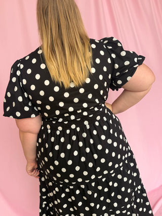 Person wearing a black dress with white polka dots against a pink background