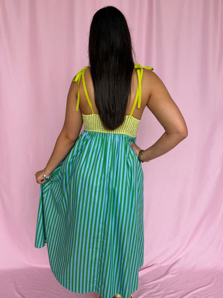 Woman wearing a green and white striped dress with a yellow top against a pink background