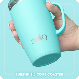 A hand holding a mint green insulated tumbler with a built-in silicone coaster, featuring the 'swig' brand logo on the front, set against a matching light blue background with text at the bottom.