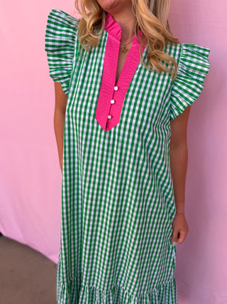 Woman wearing a green and white checkered dress with a pink tie against a pink background