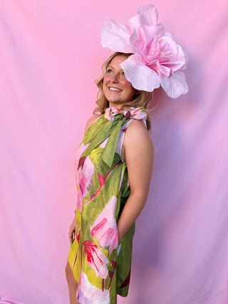 Woman wearing a colorful floral dress and large pink flower headpiece against a pink background