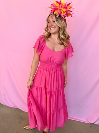 Woman wearing a pink dress and colorful headpiece against a pink background