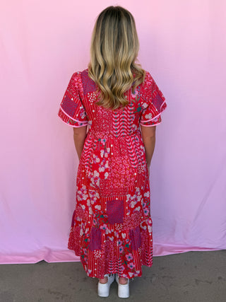 Person wearing a red floral dress against a pink background