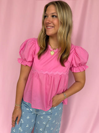 Woman wearing a pink blouse with puff sleeves against a pink background