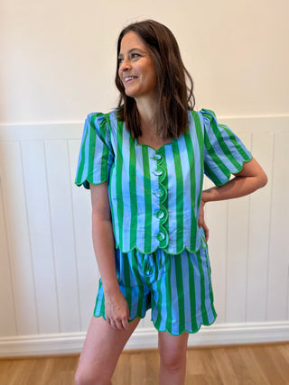 Woman wearing a green and blue striped outfit standing against a white wall.