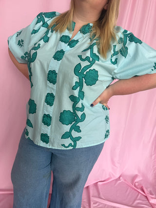 Person wearing a light blue blouse with green floral patterns against a pink background
