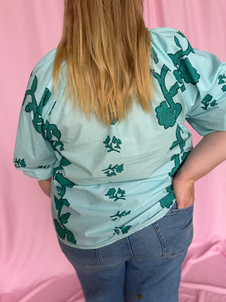 Person wearing a light blue shirt with green patterns against a pink background