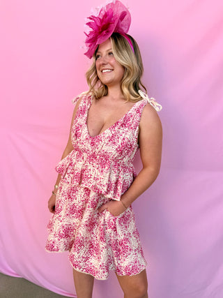 Woman wearing a pink floral dress and matching headpiece against a pink background