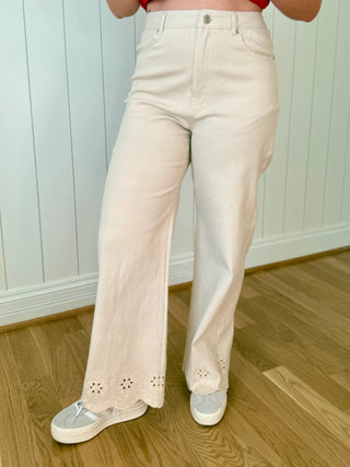 Person wearing a red top and beige pants with floral cutouts on a wooden floor.